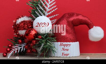 Santa hat und Weihnachten Ornamente mit ein frohes neues Jahr 2020 Nachricht auf einem festlichen roten Hintergrund Stockfoto