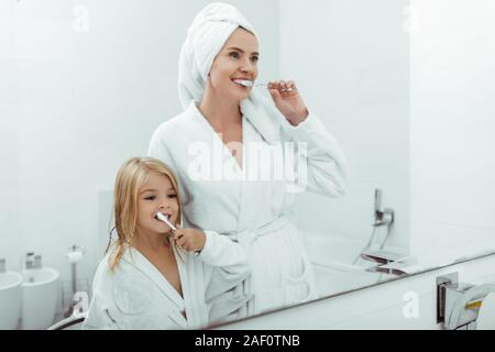 Glückliche Mutter und Tochter in bademänteln Zähneputzen in der Nähe von Spiegel Stockfoto