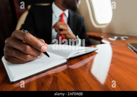 Ansicht der afrikanischen amerikanischen Mann, der die Feder in der Nähe von Notebook in Private Jet 7/8 Stockfoto