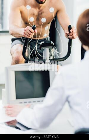 7/8-Ansicht der Arzt die Durchführung Dauertest mit Sportler mit Elektroden in der Turnhalle Stockfoto