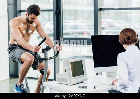 Arzt Durchführung Dauertest mit Sportler mit Elektroden in der Turnhalle Stockfoto