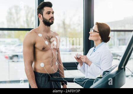 Arzt Durchführung Härtetest in der Nähe von Sportsman mit Elektroden im Sportzentrum Stockfoto