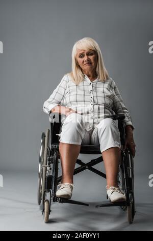 Verärgert und deaktiviert den Ruhestand Frau sitzt im Rollstuhl auf Grau Stockfoto