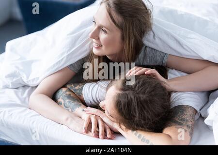 Zwei lächelnde Lesben umarmt, während unter der Decke im Bett lag, Stockfoto