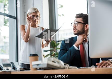 Selektiver Fokus der überrascht Geschäftsfrau am Computer Monitor in der Nähe schöner Mann suchen in Gläsern Stockfoto