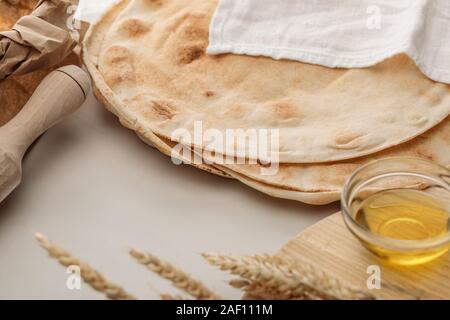 Flache lavash Brot bedeckt mit weißen Handtuch in der Nähe von Rolling Pin und Schneidbrett mit Spikes und Öl Stockfoto