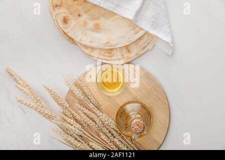 Blick von oben auf die lavash Brot mit weißen Handtuch in der Nähe von Schneidbrett mit Spikes und Öl auf Marmor Oberfläche beschichtet Stockfoto