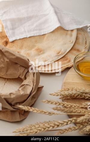 Lavash Brot mit weißen Handtuch in der Nähe von Mehl Paket abgedeckt und Schneidbrett mit Spikes und Öl Stockfoto