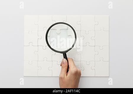 7/8-Ansicht von Frau mit Lupe unter Puzzle mit verloren gegangenen Stück auf weißem Hintergrund Stockfoto