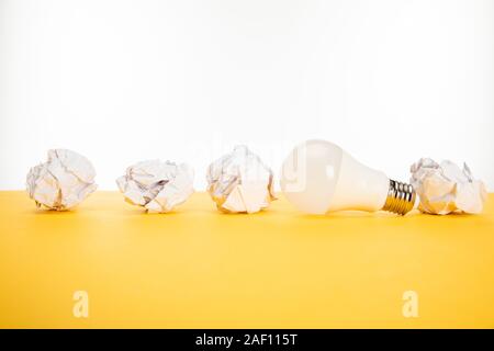 Glühbirne und zerknittertes Papier auf gelbe Oberfläche auf Weiß isoliert Stockfoto
