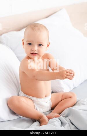 Nette blauäugige Kind sitzen auf dem Bett mit weißer Bettwäsche und Kamera Stockfoto