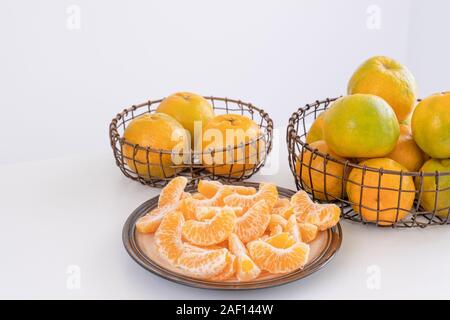 Schöne geschälte Mandarinen in eine platte und Metall Korb auf hellen, weißen sauberen Tisch in einem modernen, zeitgenössischen Küche Insel isoliert, bis zu schließen. Stockfoto
