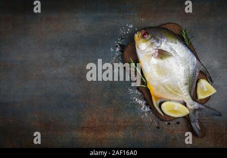 Frische butterfische Fisch mit Kräuter Gewürze Rosmarin und Zitrone auf Holz Schneidebrett und schwarze Platte Hintergrund/Raw schwarz butterfische Fisch Stockfoto