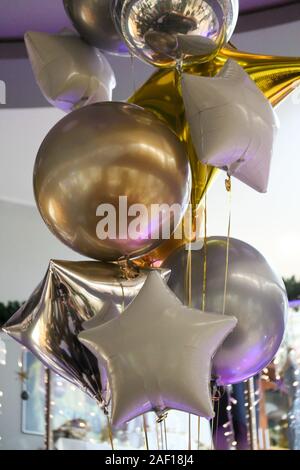 Bündel von Helium Aufblasbare Ballone auf der Party. Silber und Gold farbigen Formen von Kugeln und Sterne in der Luft hängen. Geburtstag, Silvester oder Hochzeit Stockfoto