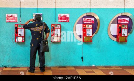 Ein asiatischer Mann über die altmodische, Münzwaschmaschinen, Druckknopf, an der Wand angebrachte payphone Systems, mit Kunststoff Handsets in Singapur. Stockfoto