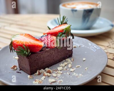 Köstliche Schokolade Torte mit Erdbeeren und Beeren auf Graue Keramik Schüssel mit heißem Kaffee Tasse auf Bambus Tisch lagen. Stockfoto