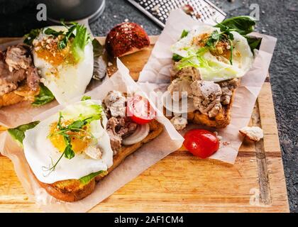 Sea Food Sandwich. Lebertran, frischem Salat, Erbsen Sprossen, Tomaten und Spiegelei. Gesundes und schmackhaftes Frühstück auf einem Holzbrett. Stockfoto