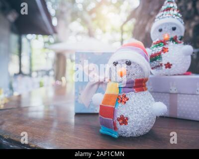 Frohe Weihnachten Hintergrund. Kleinen Niedlichen snowmans mit bunten Kleiderordnung und süßen vorhanden Boxen auf hölzernen Tisch, draußen mit kopieren. Stockfoto