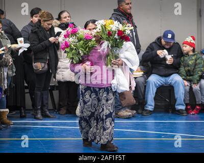 Des Moines, Iowa, USA. 11 Dez, 2019. Eine Frau trägt Blumen für ein Angebot in der Sporthalle des Unsere Damen der Americas Kirche während der Jungfrau von Guadalupe Feier in der Kirche in Des Moines. Jungfrau von Guadalupe Tag ist einer der wichtigsten heiligen Tage in mexikanischen Katholizismus. Es Markierungen, Dez. 12, 1531, der Tag, Juan Diego, der indigenen mexikanischen Bauern, sah eine Erscheinung der Jungfrau Maria auf einem kahlen Hügel in Mexiko Stadt. Eine Basilika wurde auf dem Gelände gebaut. Jungfrau von Guadalupe Tag ist in ganz Mexiko und auch in der mexikanischen Gemeinschaften in den Vereinigten Staaten gefeiert. (Credit I Stockfoto