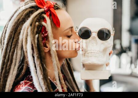 Schöne Frau mit Dreadlocks küsse einen Schädel in Sonnenbrille Stockfoto