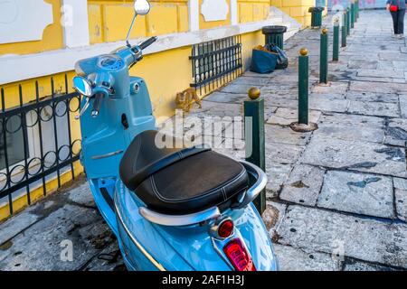 Eine streunende Katze Katze Wanderungen bis zu einem blauen Motorrad Roller im Plaka Viertel von Athen, Griechenland. Stockfoto