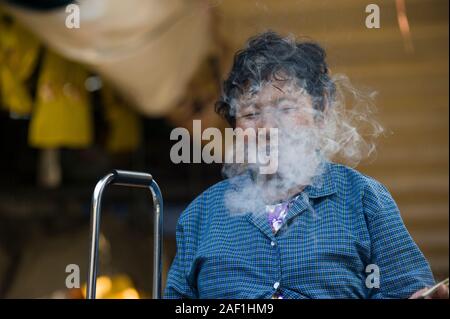 Bangkok, Thailand - 18 April 2011: Ältere Thai Frau hinter Zigarettenrauch in a Street Market in Bangkok Stockfoto