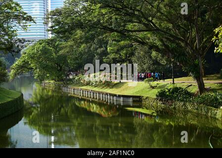 Gruppe von Menschen im Botanischen Garten läuft mit Wolkenkratzern im Hintergrund. Kuala Lumpur Stockfoto