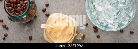 Blick von oben auf Eis Kaffee im Glas Glas mit Stroh in der Nähe von Kaffee Körner und Eiswürfel auf grauem Hintergrund, Panorama-Aufnahme ein. Stockfoto