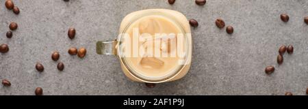 Blick von oben auf Eis Kaffee im Glas in der Nähe von Kaffee Körner auf grauem Hintergrund, Panorama-Aufnahme ein. Stockfoto