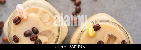 Selektiver Fokus der Eis Kaffee im Glas Glas mit Stroh in der Nähe von Kaffee Körner auf grauem Hintergrund, Panorama-Aufnahme ein. Stockfoto