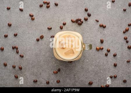 Blick von oben auf die leckeren Eis Kaffee in Glas Glas in der Nähe von Kaffee Körner auf grauem Hintergrund Stockfoto