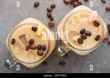 Selektiver Fokus der Eis Kaffee im Glas Glas mit Stroh in der Nähe von Kaffee Körner auf grauem Hintergrund Stockfoto