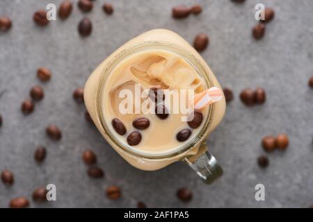 Selektiver Fokus der Eis Kaffee im Glas Glas mit Stroh in der Nähe von Kaffee Körner auf grauem Hintergrund Stockfoto