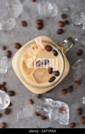 Selektiver Fokus der Eis Kaffee im Glas Glas mit Stroh in der Nähe von Kaffee Körner und Eiswürfel auf grauem Hintergrund Stockfoto