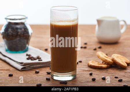 Selektiver Fokus der Eis Kaffee mit Milch in Glas in der Nähe von milchkännchen, Plätzchen und Kaffee Körner auf Holztisch isoliert auf weißem Stockfoto