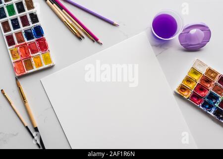 Blick von oben auf die leeren weißen Papier in der Nähe von Pinsel und Aquarellfarben auf Marmor weiß Oberfläche Stockfoto