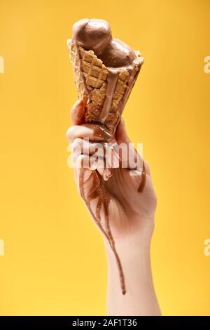 Teilweise mit Blick auf die Frau mit köstlichen geschmolzene Schokolade Eis in knuspriger Waffel Kegel isoliert auf Gelb Stockfoto
