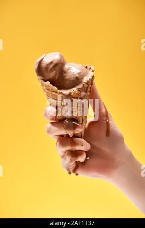7/8-Ansicht von Frau mit köstlichen geschmolzene Schokolade Eis in knuspriger Waffel Kegel isoliert auf Gelb Stockfoto