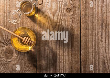 Gläser mit Honig und Honig Schöpflöffel auf Holztisch im Sonnenlicht Stockfoto