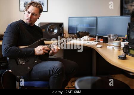 Mann mit E-Gitarre am Schreibtisch sitzen Stockfoto