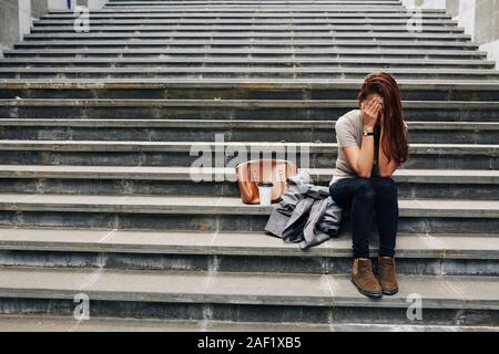 Junge Frau sitzt auf der Treppe betont neben ihrer Tasche und Jacke und Schreien nach dem fehlerhaften Prüfung Stockfoto
