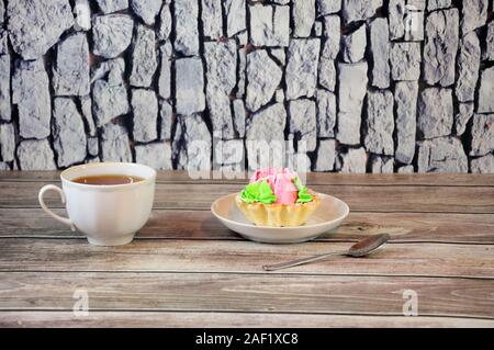 Ein weißes Porzellan Schale steht auf einem Tisch gegen die Wand, neben der gleichen Untertasse mit Kuchen in Form eines Korbes mit weißen Vanillepudding und einem Löffel. Cl Stockfoto