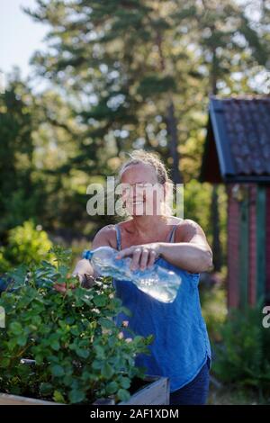 Lächelnde Frau Bewässerung Pflanzen im Garten Stockfoto