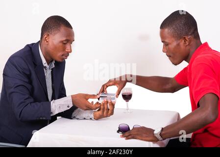 Zwei Männer, die um den Tisch poker spielen und trinken Wein sitzen. Mann in Rot schießen Karten aus einander die Hände. Stockfoto