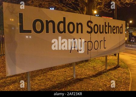 Beleuchtetes Schild am Flughafen London Southend bei Nacht, eingerahmt von Bäumen, Zäunen und Straßenlaternen in der Nähe des Terminaleingangs. Stockfoto
