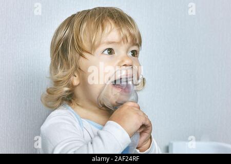 Kleine weiße nettes Mädchen mit lockigem Haar ist mit medizinischen Maske, die hilft bei Asthma oder anderen Atemwegserkrankungen, sie lächelt und c Stockfoto