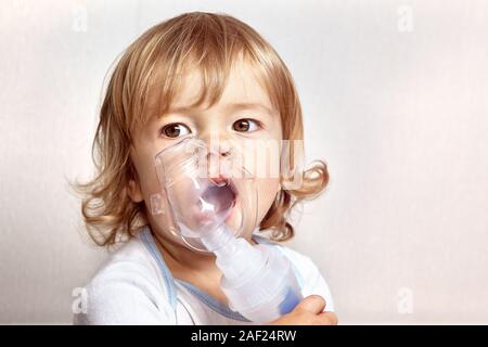 Kleine weiße kaukasische Mädchen mit blondem Haar ca. 2 Jahre alt ist, die versucht, ihr Asthma Angriff mit Hilfe von speziellen Maske zu stoppen. Sie hält es und bre Stockfoto