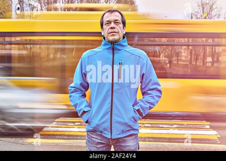 Allein weiß kaukasischen Wanderarbeitnehmer ca. 50 Jahre alt, blaue Jacke ist der Aufenthalt auf der Straße mit dem Bus auf dem Hintergrund. Er hat einen ernsten Blick, Bec Stockfoto