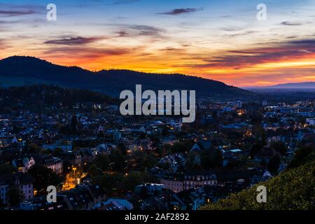 Deutschland, Magische orange sky über Freiburg im Breisgau City Skyline, Stadtbild und Häuser bei Nacht beleuchteten, Luftaufnahme über Dächer Stockfoto