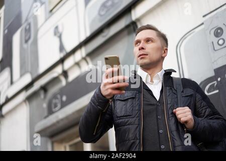Junge Menschen, die mit dem Telefon in der Hand zu Fuß in der Stadt gegen den Hintergrund der modernen Gebäuden Stockfoto